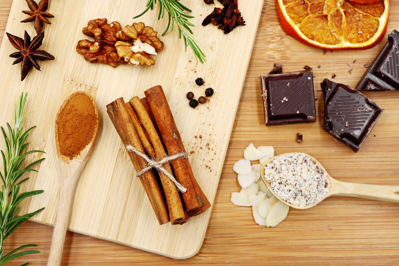 A flat lay of baking ingredients including cinnamon, dark chocolate, and walnuts on a wooden board.