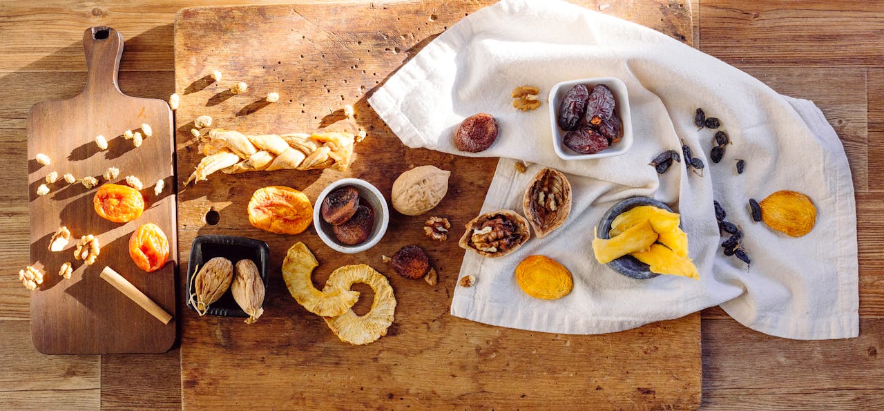 A variety of dried fruits displayed on a wooden table with cloth and cutting board.